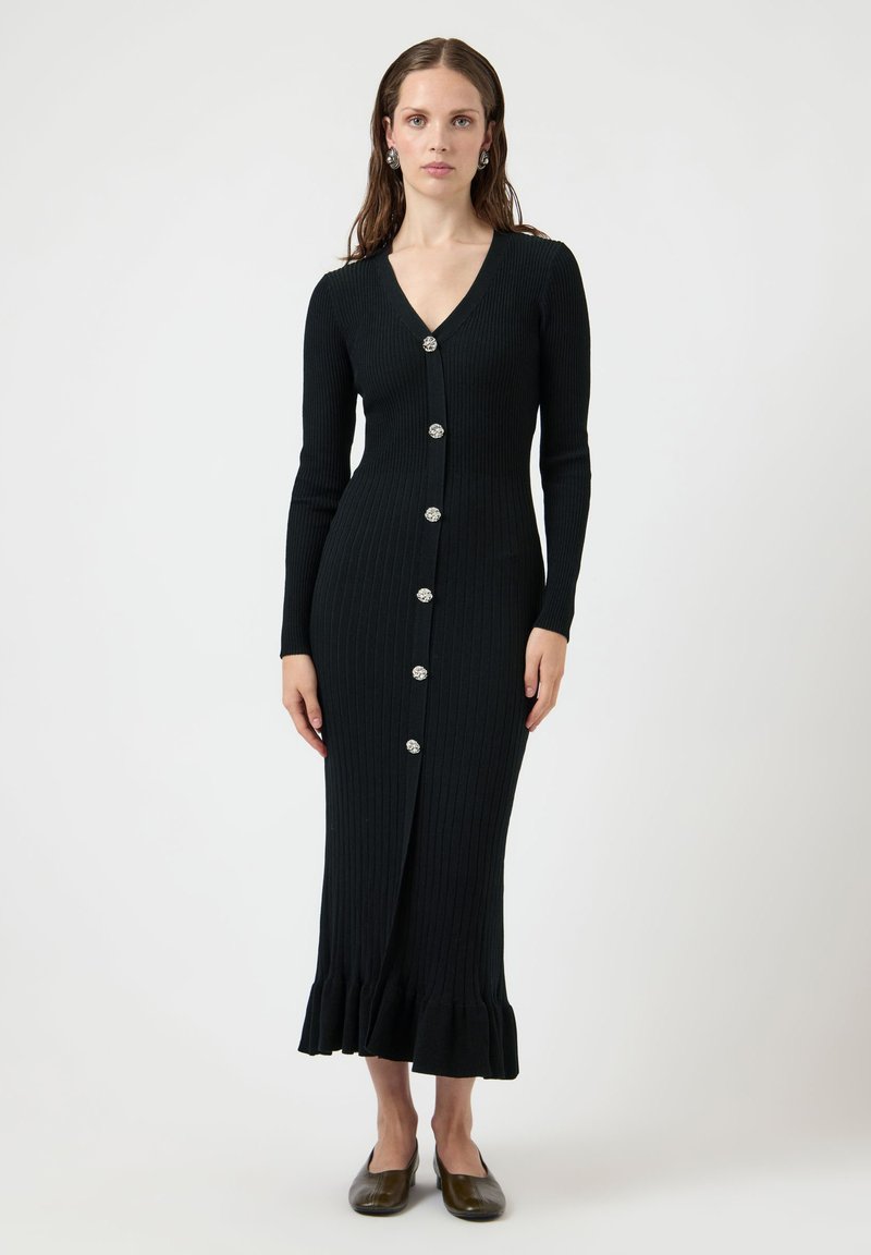 Μαύρο πλεκτό φόρεμα με ριμπ ύφανση, μακριά μανίκια και V-λαιμόκοψη, διακοσμημένο με ασημένια κουμπιά στο μπροστινό μέρος και καμπυλωτή ουρά.