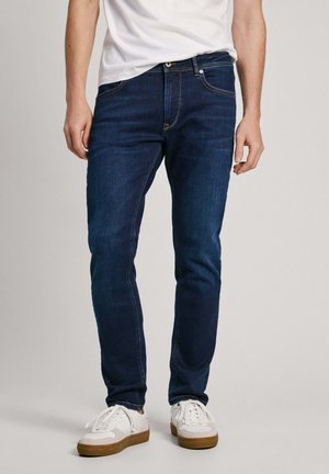 Tumedate sinised denim püksid, mis on slim fit stiilis, klassikalise viie taskuga disainiga, õmblustehnikaga ning lukuga, millel on ühe nööbiga sulgemine.