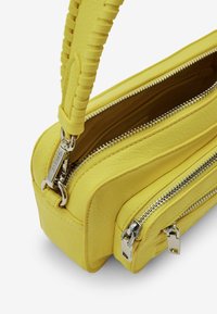 Żółta skórzana torebka o teksturowanym wykończeniu, z dwoma zamykanymi na zamek komorami oraz plecionym uchwytem. Akcenty w kolorze srebra.