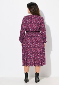 Vestido largo con estampado floral en tonos de púrpura y rosa, con mangas largas, cintura ceñida y una silueta fluida. Botines negros.