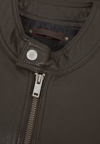 Braune Lederjacke mit Stehkragen, silbernem Reißverschluss und metallischem Druckknopfverschluss. Mit roten Akzentnähten auf dem Innenfutter.