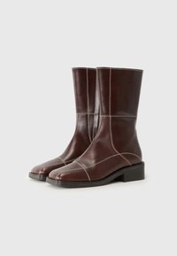 Bottes en cuir marron à chevilles avec des orteils carrés, présentant des coutures blanches contrastantes et un petit talon carré, exposées sur un fond blanc.