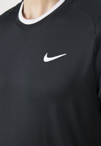 Svart trenings T-skjorte med rund hals, med en hvit Nike swoosh-logo på brystet. Glatt tekstur, slankt design.