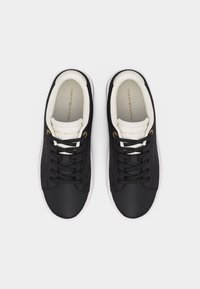 Ζευγάρι μαύρα sneakers χαμηλού ύφους με λευκές εσωτερικές επενδύσεις και σόλες, μαύρα κορδόνια και χρυσή σήμανση Tommy Hilfiger στις πλευρές και στη γλώσσα.