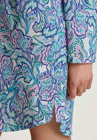 Il tessuto multicolore e decorato presenta disegni floreali vorticosi in blu, verde e rosa. Il vestito ha uno spacco laterale e una consistenza morbida.