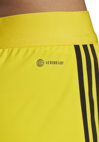 AEROREADY gelbe Sportshorts mit einem breiten Bund, schwarzen Seitenstreifen und einem dunkelblauen Logo auf der linken Seite.