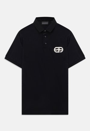 Svart kortärmad polo med tre knappar och vit broderad geometrisk logotyp på vänster bröst.