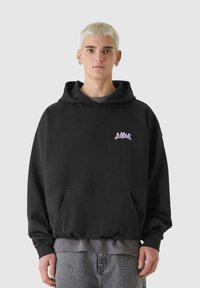 Svart huvtröja med framficka och en liten lavendel-logotyp. Mjuk tyg, avslappnad passform och ribbade ärmslut.