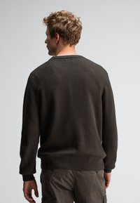 Dunkelbrauner, gerippter Strickpullover mit Rundhalsausschnitt, langen Ärmeln und figurbetontem Saum, kombiniert mit grauen Cargo-Hosen.