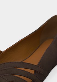 Κοντινό πλάνο καφέ επίπεδου παπουτσιού με λείο εσωτερικό και επικαλυπτόμενα οριζόντια λουράκια κοντά στην περιοχή των δαχτύλων.