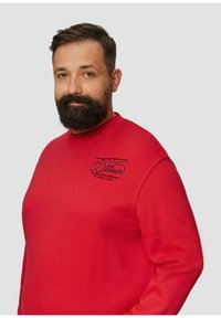 Sweat-shirt rouge avec col rond et manches longues. Présente un logo en texte noir sur la poitrine. Fabriqué en tissu doux et texturé.