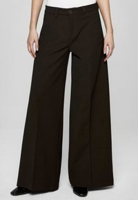 Brązowe spodnie o szerokich nogawkach wykonane z teksturowanej tkaniny, z zapięciem na guzik i szlufkami na pasek, o czystej, dopasowanej sylwetce.