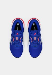 Par blå atletiske løpesko med hvite såler, røde detaljer og svarte innleggssåler med merkevare, sett ovenfra på hvit bakgrunn.