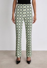 Gemusterte Hosen in Hellgrün mit schwarzen und cremefarbenen geometrischen Designs. Hergestellt aus einem glatten Stoff, mit tailliertem Schnitt und ausgestelltem Bein.