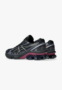 Scarpe sportive nere e grigie con tomaia in rete, strisce di accento argentate e suola spessa viola con ammortizzazione in gel.