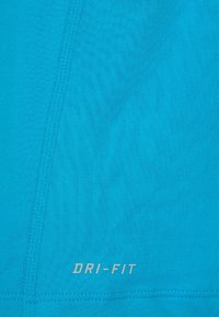 Tyrkysová DRI-FIT látka s hladkým povrchem. Obsahuje jemné švy a výrazné tištěné logo ve stříbrné barvě. Lehký sportovní design.