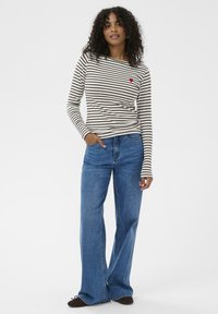 Gestreiftes Langarm-T-Shirt in Beige und Dunkelbraun mit einem kleinen roten Herzdetail; kombiniert mit schmalen blauen Jeans.