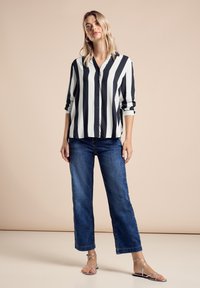 Schwarz-weiß gestreiftes Hemd mit langen Ärmeln, kombiniert mit blauen, weit geschnittenen Jeans und silbernen, trägerlosen Sandalen.