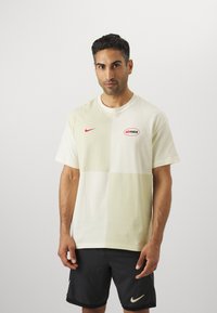 Kreemja ja helesinise värvi plokkkärbiga T-särk, mille materjaliks on puuvill, esiküljel on punane Nike logo ja ringikujuline "aimax" bränding.