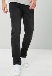 Slim-fit mustat farkut, joissa on sileä pinta. Varustettu klassisella viiden taskun suunnittelulla ja esitelty valkoisten lenkkarien kanssa.