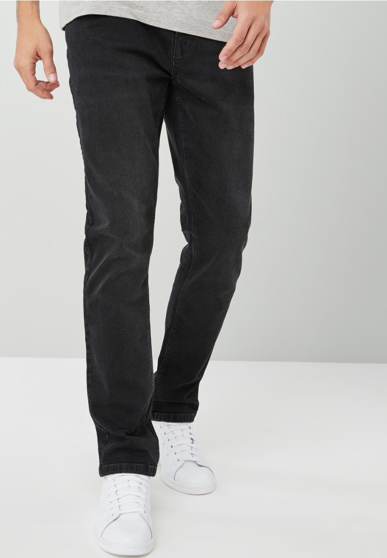 Slim-fit mustat farkut, joissa on sileä pinta. Varustettu klassisella viiden taskun suunnittelulla ja esitelty valkoisten lenkkarien kanssa.