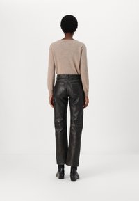 Pantaloni din piele neagră cu croială dreaptă, având buzunare din spate și cusături galbene, asociați cu un pulover de culoare maro deschis.