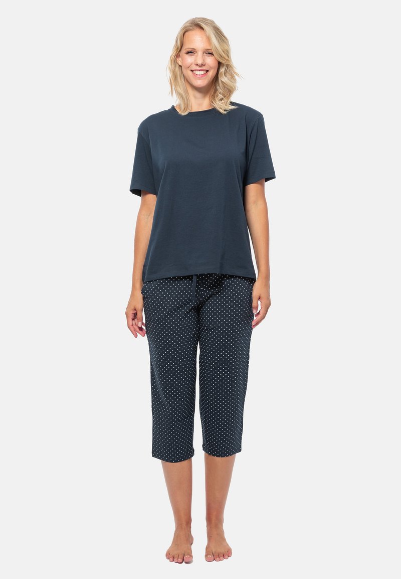 Navyblaue Baumwoll-T-Shirt mit kurzen Ärmeln, kombiniert mit cropped Hosen im weißen Polka-Dot-Muster. Weicher Stoff, lockerer Schnitt.