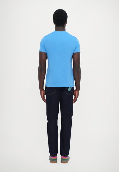 Tricou albastru cu mânecă scurtă, blugi denim închis și adidași multicolori. Design simplu, formă ajustată, textură netedă și fără modele vizibile.