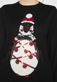 Maglione nero con design di pinguino realizzato in paillettes. Il pinguino indossa un cappello rosso, ha un ventre bianco e dettagli rossi, con una trama lavorata a maglia.