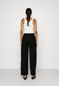 Zwarte wijde broek met een aansluitende taille en achterzakken, gecombineerd met een witte tanktop. Soepele textuur en minimalistisch ontwerp.
