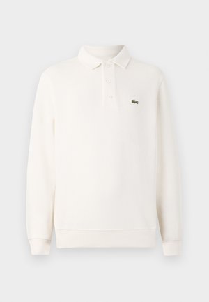 Polo de culoare crem deschis, cu mânecă lungă, realizat dintr-un tricot texturat, având o închidere cu trei nasturi și un logo brodat verde pe piept.