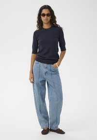 Marineblaues, geripptes Strick-Top mit kurzen Ärmeln, kombiniert mit hellblauen, locker sitzenden Jeans und braunen Loafers. Einfaches Design mit entspannter Silhouette.