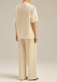 Beżowy, teksturowany, dwuczęściowy zestaw składający się z bluzki z krótkim rękawem oraz spodni z szerokimi nogawkami w falisty wzór. Miękka tkanina i luźny krój.