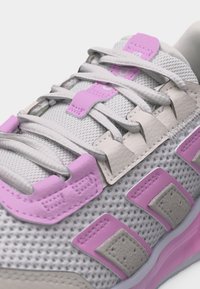 Κοντινό πλάνο σε λευκό αθλητικό παπούτσι από δίχτυ με ροζ και μπεζ δερμάτινες λεπτομέρειες και λευκά κορδόνια περασμένα από τριγωνικά περάσματα.