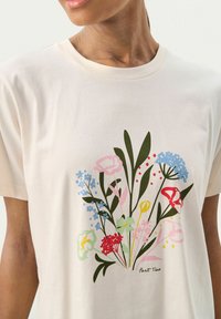 T-shirt de couleur crème en tissu doux, avec un imprimé floral en rose, bleu, vert et rouge, portant le texte "Part Two" en bas.