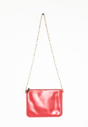 Sac banane en cuir rouge brillant avec bandoulière en chaîne dorée et petite tirette de fermeture éclair, marqué "Tommy Hilfiger" en texte blanc sur le devant.