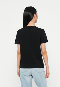 Μαύρο κοντομάνικο βαμβακερό μπλουζάκι με κλασικό λαιμόκοψη τύπου crew και άνετη εφαρμογή, συνδυασμένο με ελαφρώς μπλε τζιν παντελόνι.