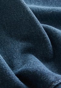 Tumedat sinised kangad, millel on pehme tekstuur, sisaldavad peent kudumisvormi ja õrnaid voldikesi, mis loovad sügavuse tunde.