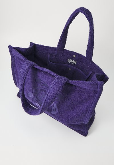 Lila Frottee-Tasche mit zwei Griffen, einer Innen pocket und einem strukturierten Logodesign auf der Außenseite.
