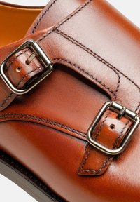 Braunes Leder-Schuh mit einem doppelten Schnallenriemen, glatter Oberfläche und kontrastierenden Nähten, in einer schlanken, abgerundeten Form.