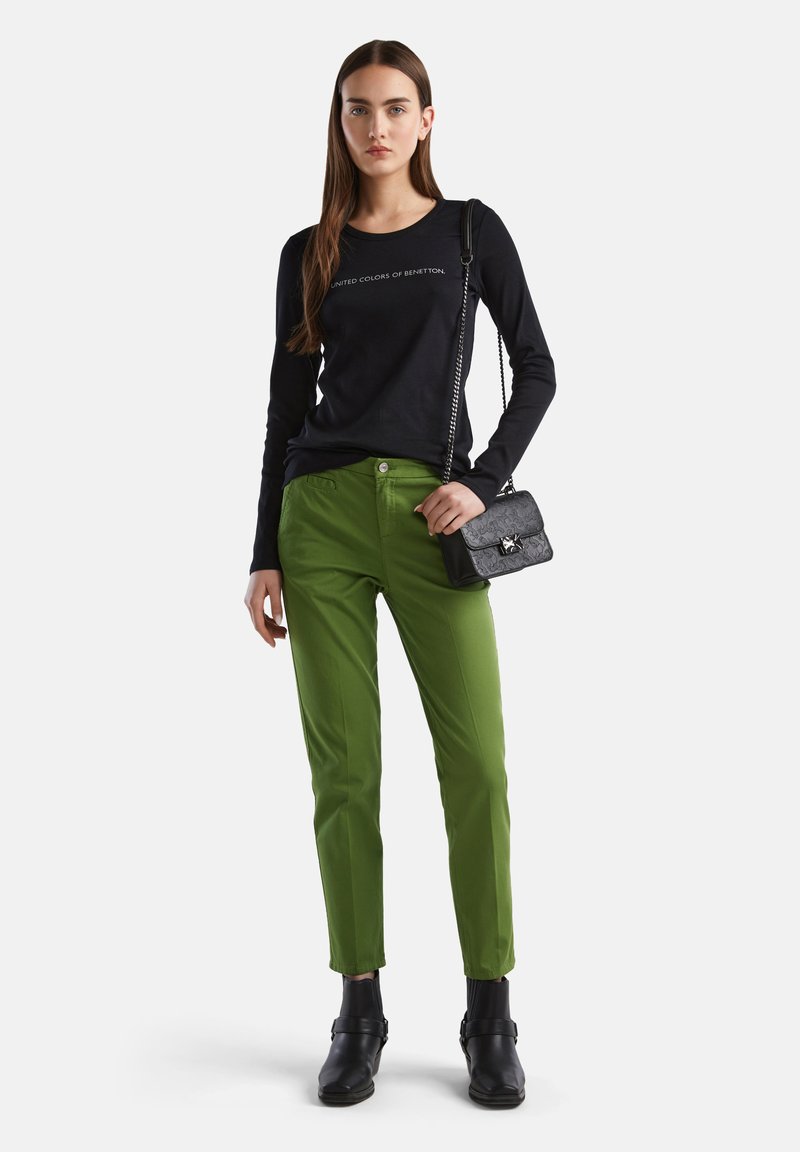 Chemise noire à manches longues avec le texte "United Colors of Benetton", associée à un pantalon droit vert et des bottines en cuir noires.