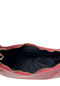 Czerwona skórzana torebka z złotym zamkiem, z czarną wyściółką wewnętrzną. Widok otwarty ukazuje przestrzenny, niestrukturalny kształt bez widocznych przegródek.