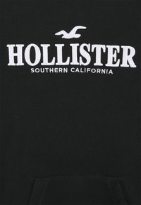 Felpa nera con cappuccio caratterizzata da un ricamo bianco con la scritta "HOLLISTER" e "SOUTHERN CALIFORNIA" sottostante. Include una tasca frontale e una texture morbida.