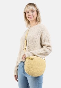 Borsa rotonda gialla con superficie morbida e testurizzata e dettagli in pelle. Presenta una tracolla rimovibile e hardware in metallo.