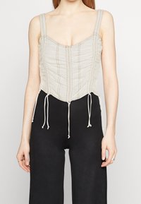 Ljust beige korsettopp med vertikal ruching, justerbara snören i midjan och tunna band. Har sydda detaljer genom hela plagget.