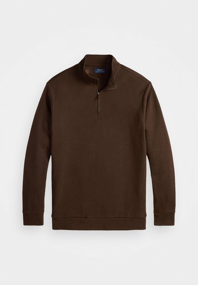 Bruine ritsloze pullover met een hoge kraag, lange mouwen en een subtiele logo-detail op de borst, gemaakt van een zacht materiaal.