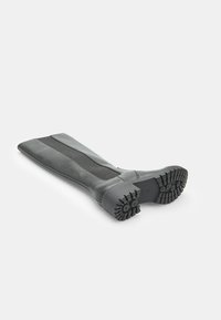 Stivale nero al ginocchio con suola in gomma spessa e pannello laterale elasticizzato, mostrato sdraiato su un lato su uno sfondo bianco.