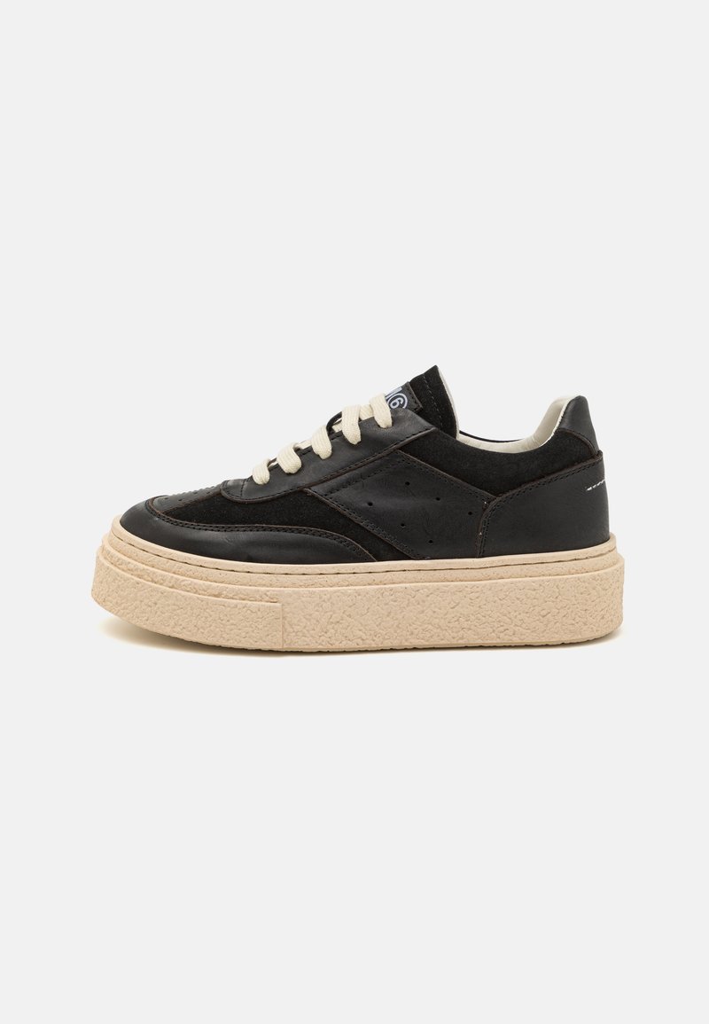 Svart lädersneaker med en texturerad beige plattformssula, krämfärgade snören och perforerad detaljering nära sidorna.