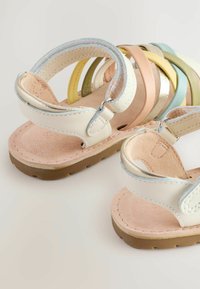 Sandalias de cuero blanco con una plantilla de ante, que presentan correas coloridas en tonos pastel y acentos metálicos. Suela de goma liviana.