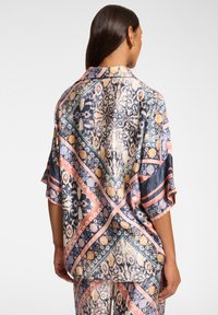 Musterndes Kimono-ähnliches Kleidungsstück aus seidig glänzendem Stoff. Verfügt über geometrische Designs in Blau, Rosa und Gold, mit lockeren, fließenden Ärmeln und seitlichen Schlitzen.